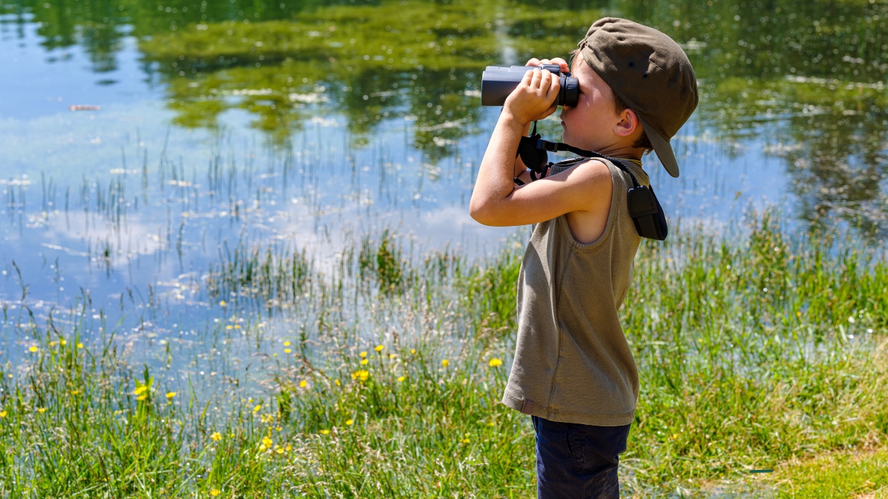 little kid with binoculars lookout out over water